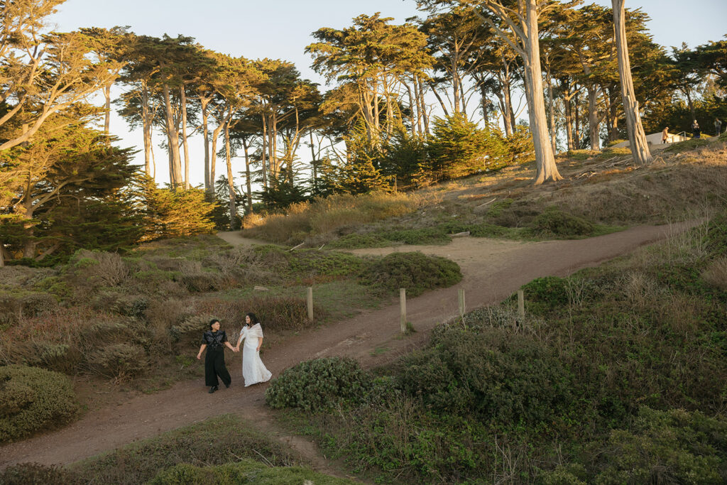 a wedding couple holding hands and walking down a hill at a park