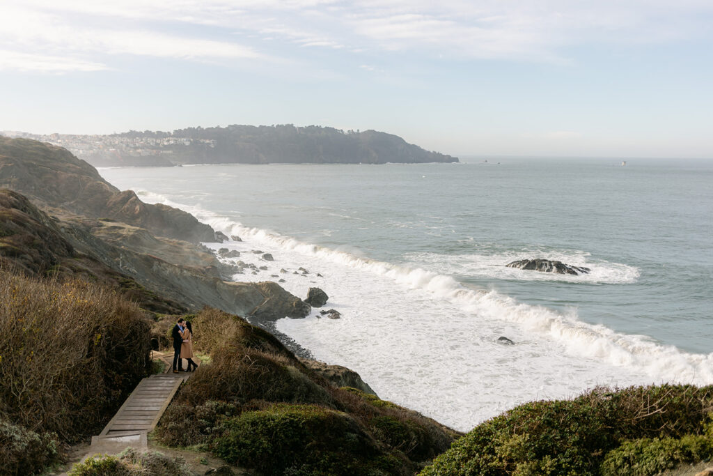a couple kissing along a trail next to the ocean