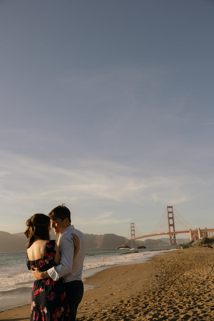 a couple embraced on the beach with the golden gate bridge in the distance