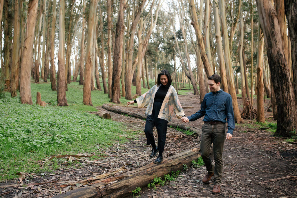 a couple holding hands and walking through a row of eucalyptus trees