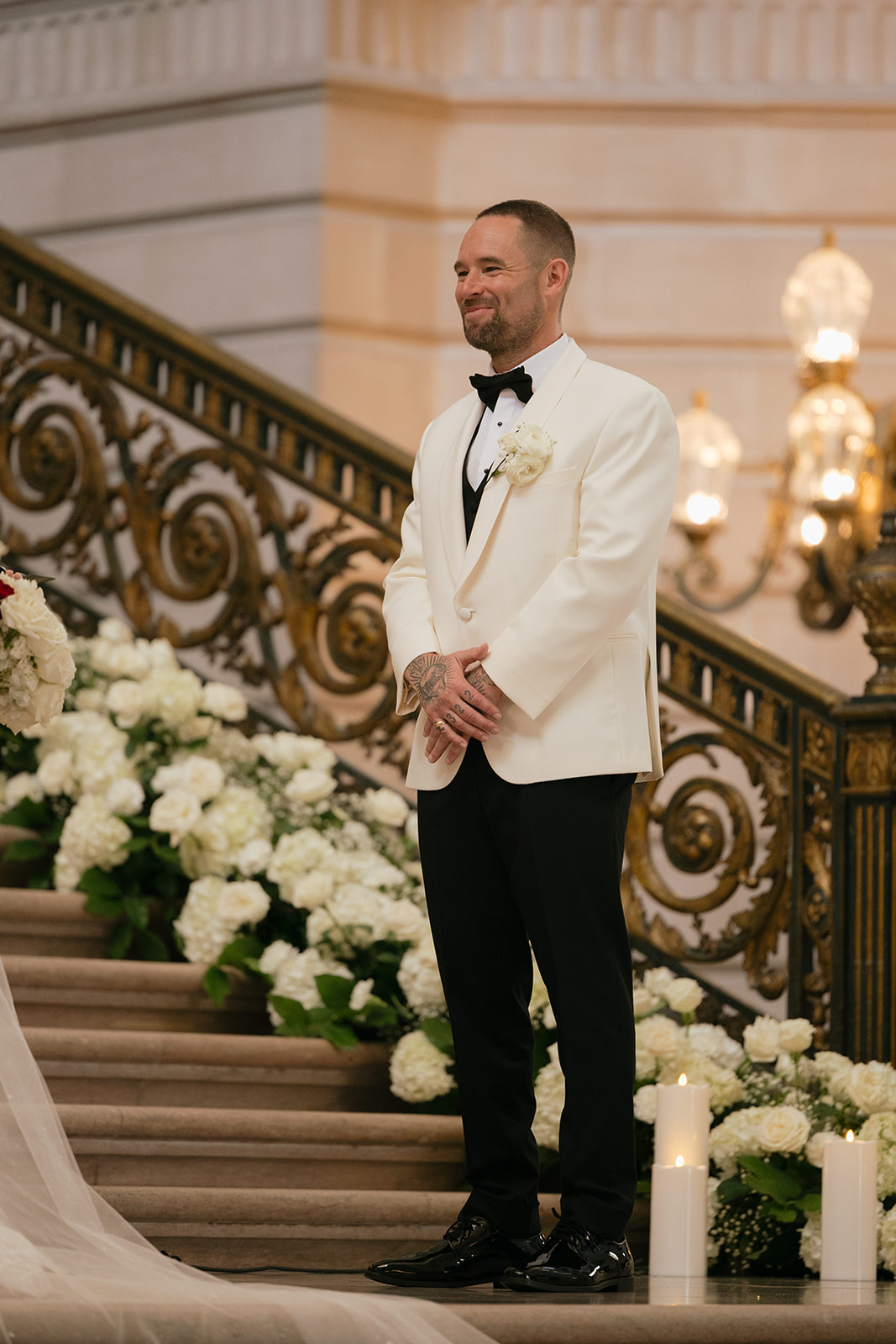 a groom standing on the grand staircase of san francisco city hall looking at his bride 
