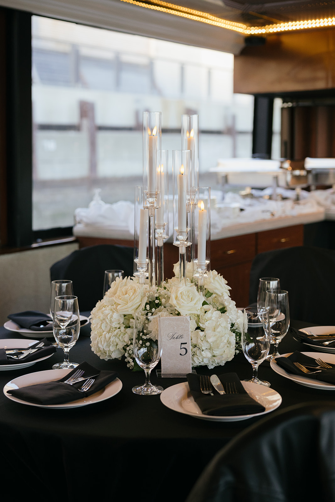 a table draped in a black tablecloth covered in candles, flowers, and plates set up for a wedding reception on a yacht